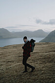 Mann wandert auf Grashügel über Fluss, Klakkur, Klaksvik, Färöer Inseln