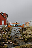 Man with backpack crossing small bridge in village, Gjogv, Eysturoy, Faroe Islands\n