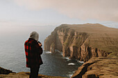 Photographer on top of rugged cliffs over ocean, Asmundarstakkur, Suduroy, Faroe Islands\n