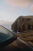 Majestic cliffs over ocean behind car, Asmundarstakkur, Suduroy, Faroe Islands\n