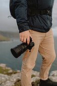 Close up hiker holding SLR camera on cliff, Neist Point, Isle of Skye, Scotland\n