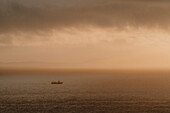 Silhouetted boat on tranquil ocean at sunset, Neist Point, Isle of Skye, Scotland\n