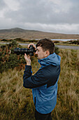 Male photographer using SLR camera in grassy field, Durness, Scottish Highlands, Scotland\n
