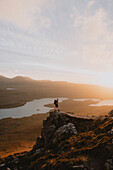 Wanderer auf zerklüftetem Berg mit Blick auf eine malerische Aussicht bei Sonnenuntergang, Assynt, Sutherland, Schottland