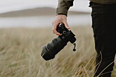 Close up photographer holding SLR camera in field\n