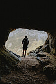 Male hiker standing in entrance of rugged mountain cave, Assynt, Sutherland, Scotland\n
