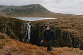 Männlicher Fotograf wandert entlang eines malerischen Wasserfalls in den Bergen, Assynt, Sutherland, Schottland