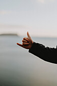 Nahaufnahme der Hand eines Mannes, der am Strand einen Shaka gestikuliert