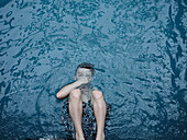 View from above boy swimming, holding breath under water surface\n