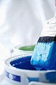 Close up of blue paint pot and dripping paintbrush\n