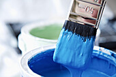 Close up of blue paint pot and dripping paintbrush\n