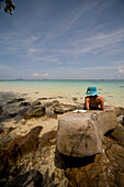 Young woman lying on rocks sunbathing and relaxing, Koh Phi Phi, Thailand\n