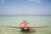 Junge Frau schwimmt mit ausgebreiteten Armen im kristallklaren Meerwasser, Koh Phi Phi, Thailand