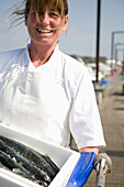 Portrait of smiling fishmonger holding a white container full of fish\n