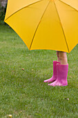 Young girl in pink boots under yellow umbrella\n