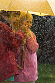 Zwei junge Mädchen im Regen unter gelbem Regenschirm