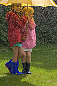 Two young girls in the rain under yellow umbrella\n