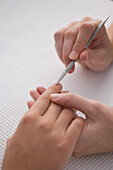 Close up of manicurist's hand pushing woman's cuticles with cuticle pusher\n