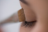 Close up of young woman eye with eyeshadow brush\n