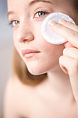 Close up of young woman removing make up with white cotton pad\n