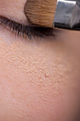 Woman applying eye make-up with eyeshadow brush and makeup powder under eye\n