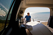 Portrait of a young man sitting with his back to the ocean shot from inside car\n