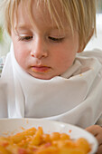 Close up of young blonde boy looking at a bowl of pasta\n
