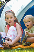 Porträt eines Jungen und eines Mädchens, die am Zelt sitzen