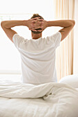 Young man sitting in bed stretching\n