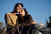 Portrait of couple embracing sitting on field\n