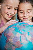 Two young girls touching and spinning  a world globe\n