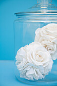 Close up of two fabric white roses in a clear glass jar\n