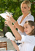 Mother and daughter setting table and polishing glasses, Italy\n