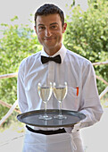 Kellner steht und hält Tablett mit zwei Gläsern Weißwein