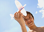 Young boy holding model aeroplane against blue sky\n