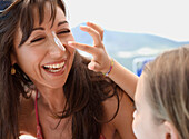 Daughter applying sunscreen lotion on mother nose\n
