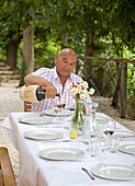 Senior sitzt am Kopf des Tisches und schenkt Rotwein ein