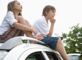 Brother and sister sitting on top of car waiting\n