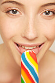 Young woman smiling and eating multicolored popsicle ice-lolly\n