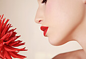Close up of young beautiful woman inhaling red dahlia\n