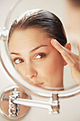 Close up of a young woman looking into round mirror checking her face\n