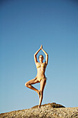 Porträt einer jungen Frau in der Baumpose des Yoga vor blauem Himmel