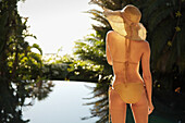 Back of young woman standing by exotic swimming pool\n