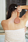Back of young woman wrapped in towel exfoliating with brush\n