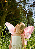 Portrait of a young girl in a fairy costume standing in a garden looking up\n