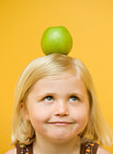 Girl with a green apple on top of her head looking up\n