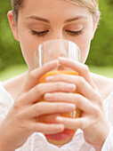 Close up of a young woman drinking and holding a glass of orange juice\n
