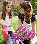 Mother and daughter kneeling in the garden tending plants and smiling\n