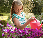 Portrait of a young girl watering flowers with pink watering can\n