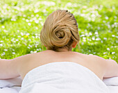 Back view of woman lying on stomach on the grass wrapped in a towel\n